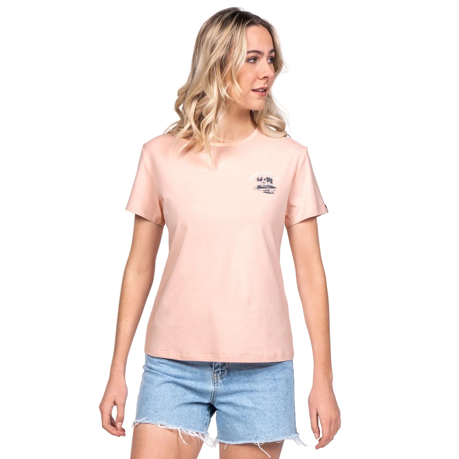 A woman modeling a pink crew neck t-shirt with a small text logo on the chest, paired with denim shorts.