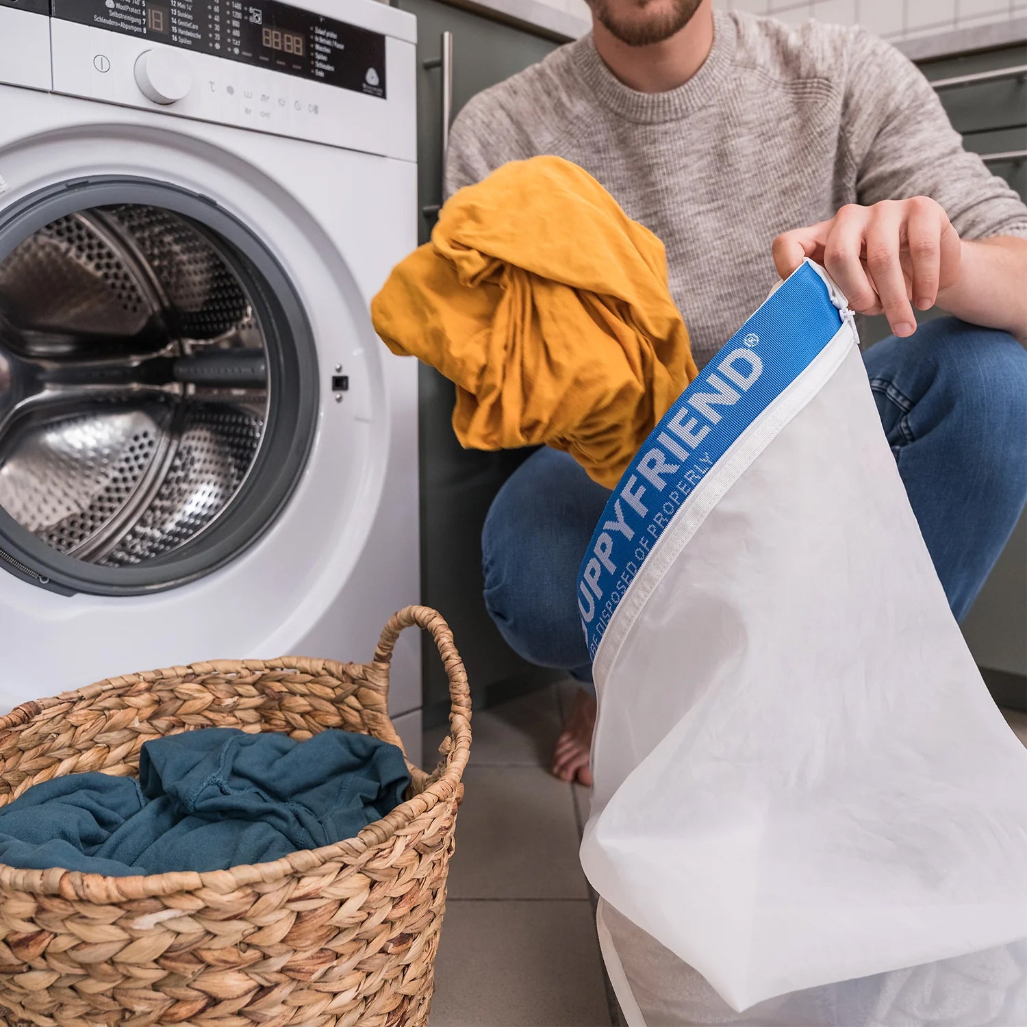 Person holding a laundry bag with a washing machine and basket of clothes in the background